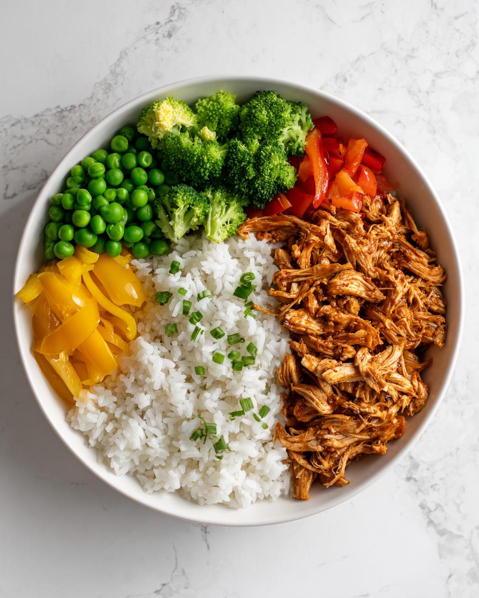 Overhead view of a colorful Chicken Meal Prep Bowls featuring shredded chicken, white rice, peas, broccoli, and peppers.