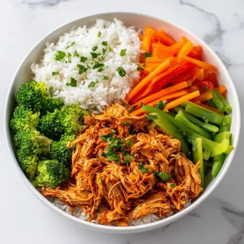 A vibrant Chicken Meal Prep Bowls featuring shredded saucy chicken, white rice, steamed broccoli, and sliced bell peppers.