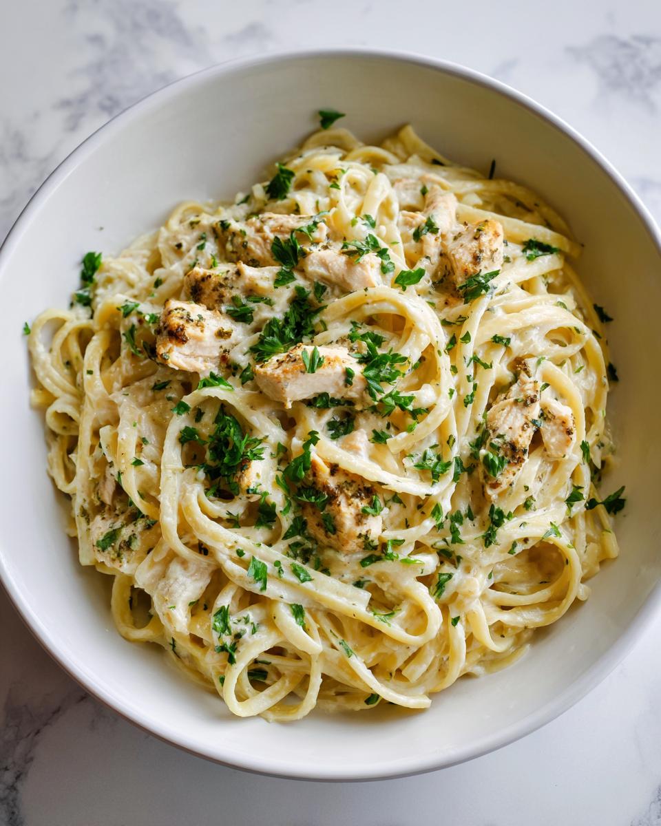 Close-up of a white bowl filled with Creamy Chicken Alfredo (Food Babe Style), topped with seasoned chicken pieces and fresh parsley.