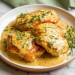 Three golden-brown chicken breasts smothered in a rich, creamy Dijon mustard sauce and garnished with fresh thyme.