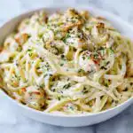 Close-up of a white bowl filled with rich Creamy Garlic Chicken Pasta, topped with herbs.