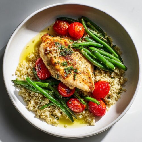 A bowl featuring a perfectly cooked chicken breast over quinoa, served with green beans and roasted cherry tomatoes, perfect for an Easy Healthy Summer Dinner.