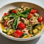 A bowl of Easy Summer Crockpot Chicken featuring shredded meat, cherry tomatoes, zucchini, and fresh basil garnish.