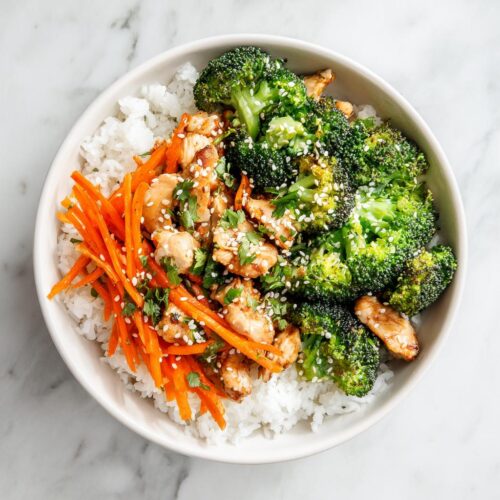 Overhead view of an Easy Summer Dinner Bowl featuring white rice, chicken pieces, bright green broccoli, and shredded carrots, topped with sesame seeds.