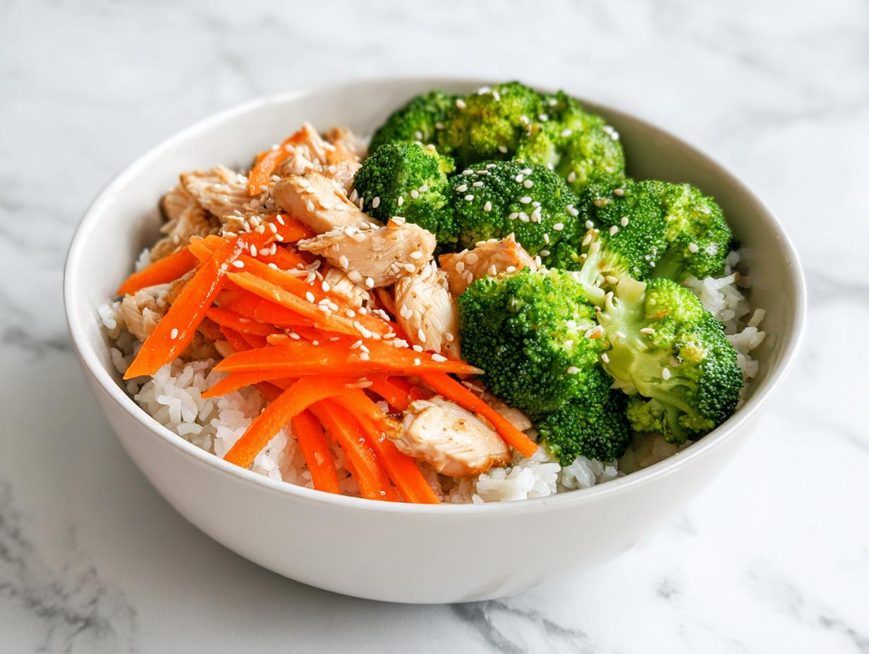 Close-up of an Easy Summer Dinner Bowl featuring white rice topped with sliced chicken, bright green broccoli, and julienned carrots, sprinkled with sesame seeds.