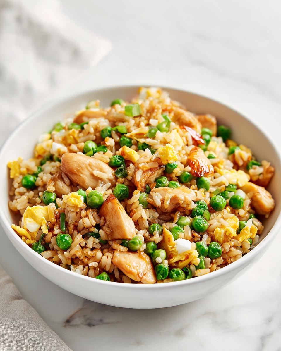 Close-up of a white bowl filled with chicken fried rice, featuring peas, scrambled egg, and green onions, perfect for an Easy Summer Rice Dinner.