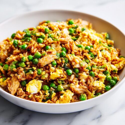 A close-up of a white bowl filled with flavorful chicken fried rice, featuring bright green peas and scrambled egg pieces, perfect for an Easy Summer Rice Dinner.