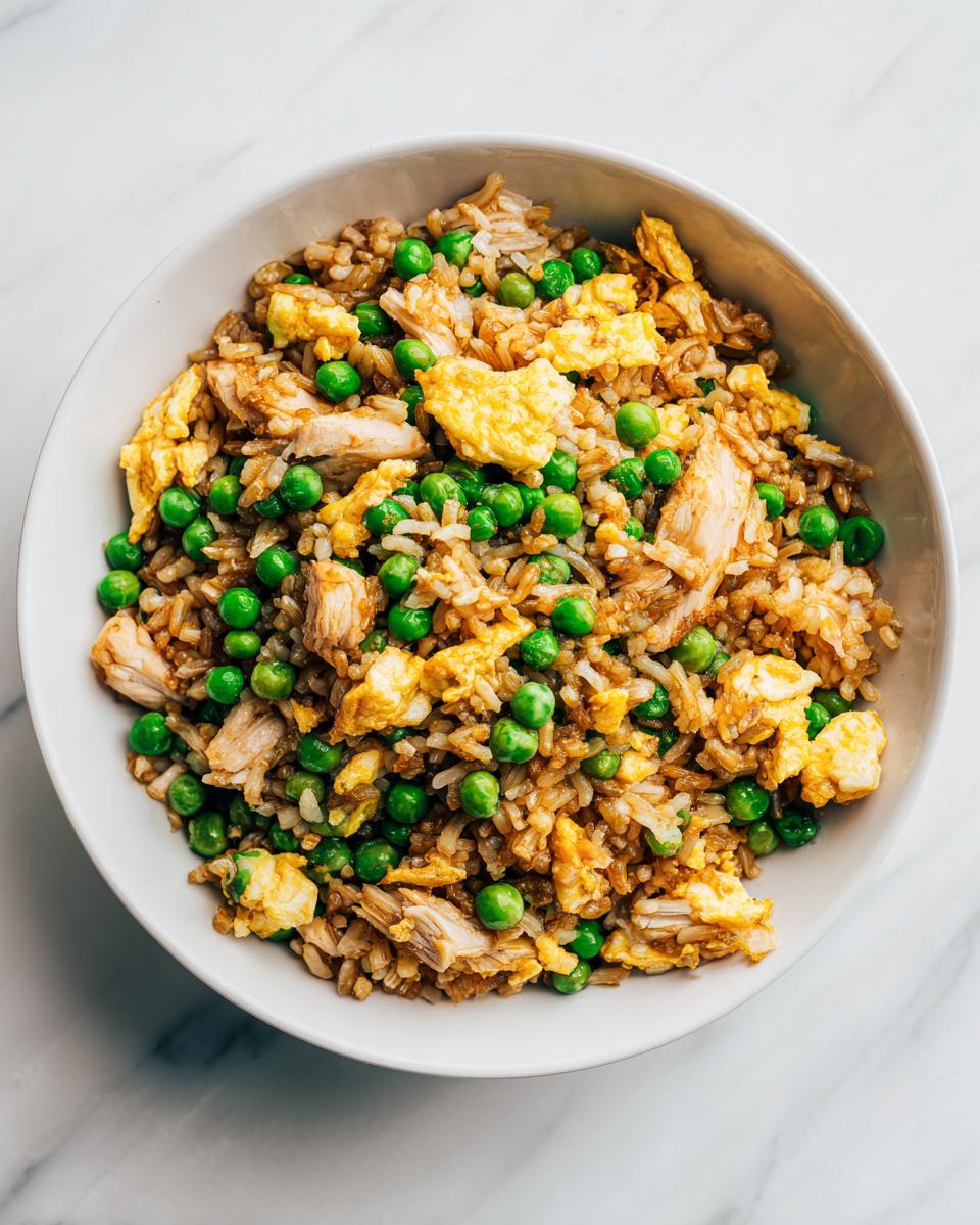 Overhead view of a bowl of Easy Summer Rice Dinner featuring fried rice with chicken pieces, scrambled egg, and bright green peas.