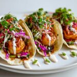 Three vibrant Easy Summer Shrimp Tacos filled with seasoned shrimp, colorful slaw, and drizzled with white sauce.