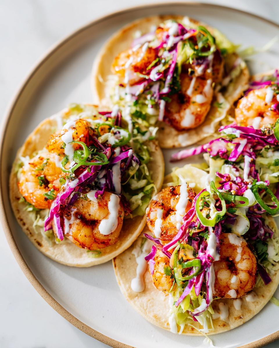 Four vibrant Easy Summer Shrimp Tacos topped with grilled shrimp, purple cabbage slaw, and white crema sauce.