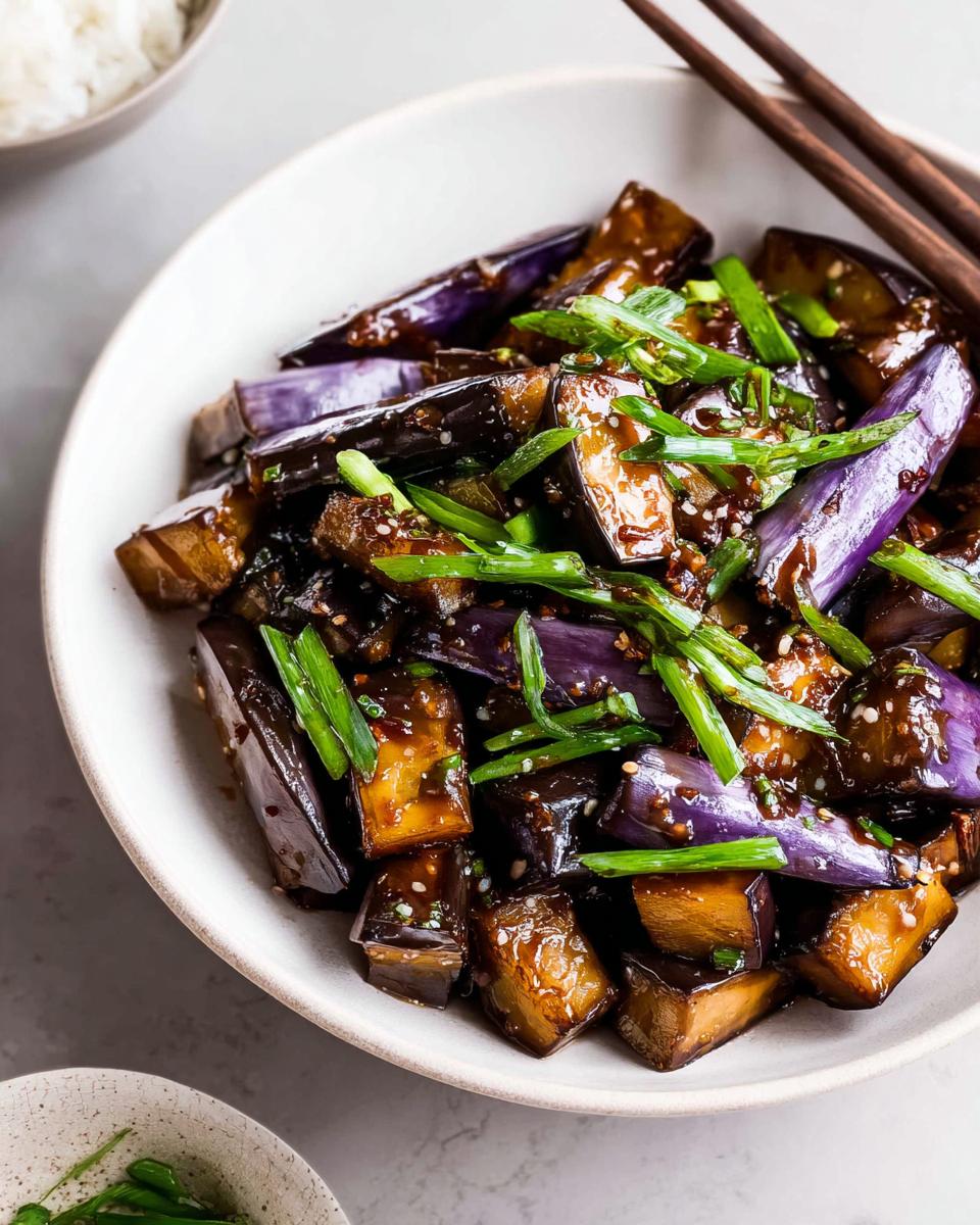 Close-up of glossy Eggplant Stir Fry Asian Style pieces topped with bright green scallions and sesame seeds.
