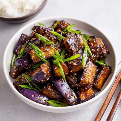 A close-up of glossy, saucy Eggplant Stir Fry Asian Style garnished with green onions and sesame seeds.