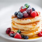 A stack of fluffy pancakes topped with mixed berries, powdered sugar, and drizzled with syrup, perfect for an Aesthetic Pancake Breakfast.