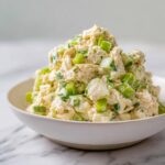 A generous serving of Fresh Summer Chicken Salad piled high in a white bowl on a marble surface.