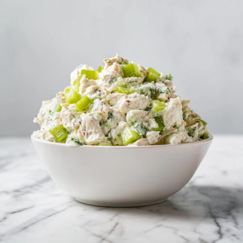 A white bowl generously filled with creamy Fresh Summer Chicken Salad, topped with bright green celery chunks.