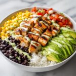 A close-up of a Fresh Summer Taco Bowl featuring grilled chicken, avocado, black beans, corn, and cilantro dressing over rice.