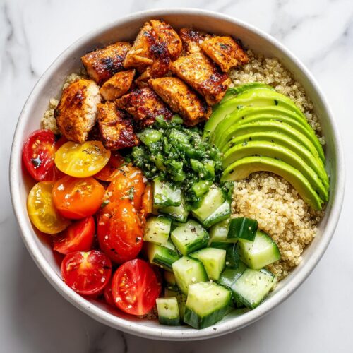 Overhead view of a Fresh Summer Veggie Chicken Bowl featuring seasoned chicken, quinoa, sliced avocado, cucumbers, and cherry tomatoes.