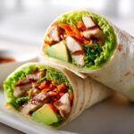 Two halves of a fresh wrap filled with grilled chicken, avocado, lettuce, and shredded carrots, showcasing great Summer Chicken Wrap Ideas.