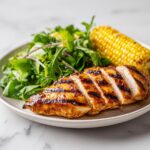A perfectly sliced Grilled Chicken Summer Plate featuring glazed chicken breast, a side of fresh greens, and grilled corn on the cob.