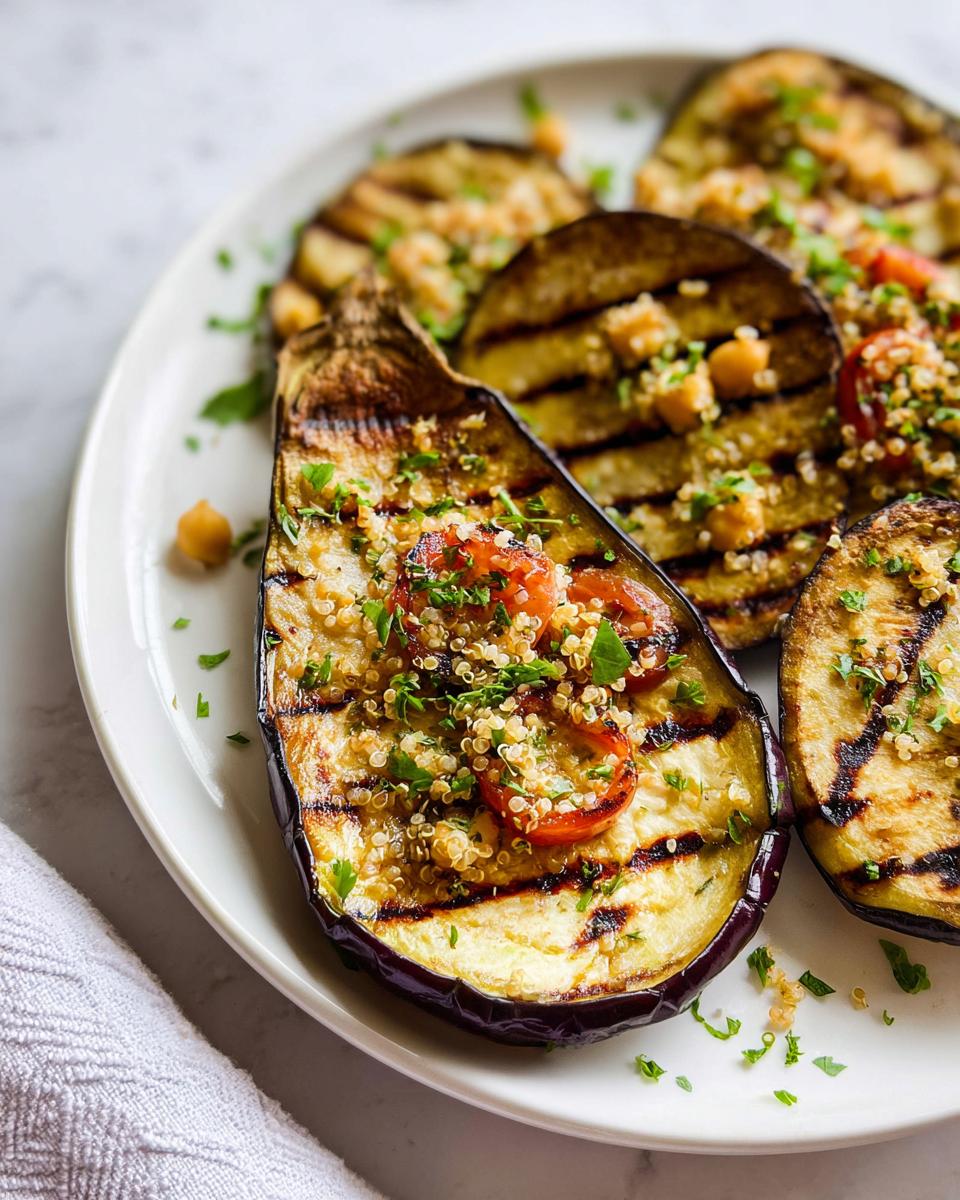 Close-up of Grilled Eggplant with Herbs halves topped with quinoa, cherry tomatoes, and chickpeas on a white plate.