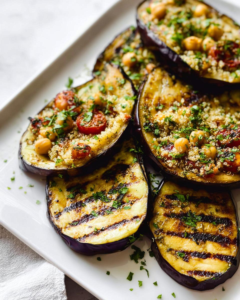 Slices of perfectly Grilled Eggplant with Herbs, topped with quinoa, chickpeas, and tomatoes.