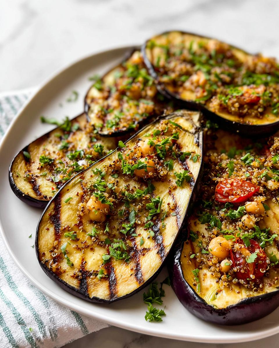 Close-up of perfectly Grilled Eggplant with Herbs, topped with quinoa, chickpeas, and tomatoes on a white plate.