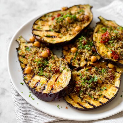 Close-up of perfectly Grilled Eggplant with Herbs, topped with quinoa and chickpeas on a white plate.
