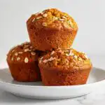 Three golden brown Healthy Banana Breakfast Muffins topped with rolled oats, stacked on a white plate.