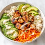 A close-up overhead shot of a Healthy Summer Chicken Bowl featuring grilled chicken, brown rice, sliced cucumber, shredded carrots, avocado, and a creamy dressing.
