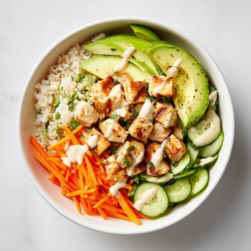 Overhead view of a Healthy Summer Chicken Bowl featuring grilled chicken, avocado, carrots, cucumber, and rice with a light dressing.