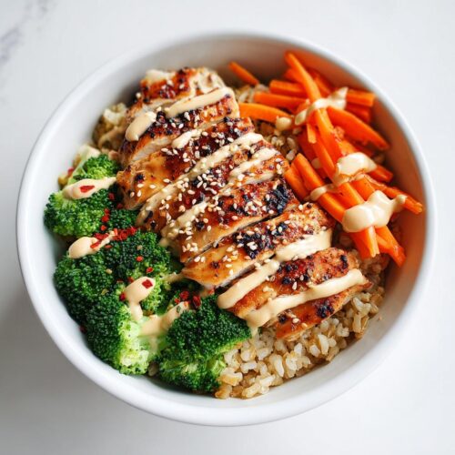 A close-up of a Healthy Summer Protein Bowl featuring sliced grilled chicken, brown rice, steamed broccoli, and julienned carrots with a creamy drizzle.