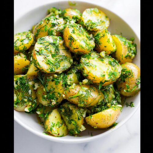 Close-up of vibrant Herb Potato Salad with Olive Oil, featuring halved yellow potatoes generously coated in fresh green herbs.