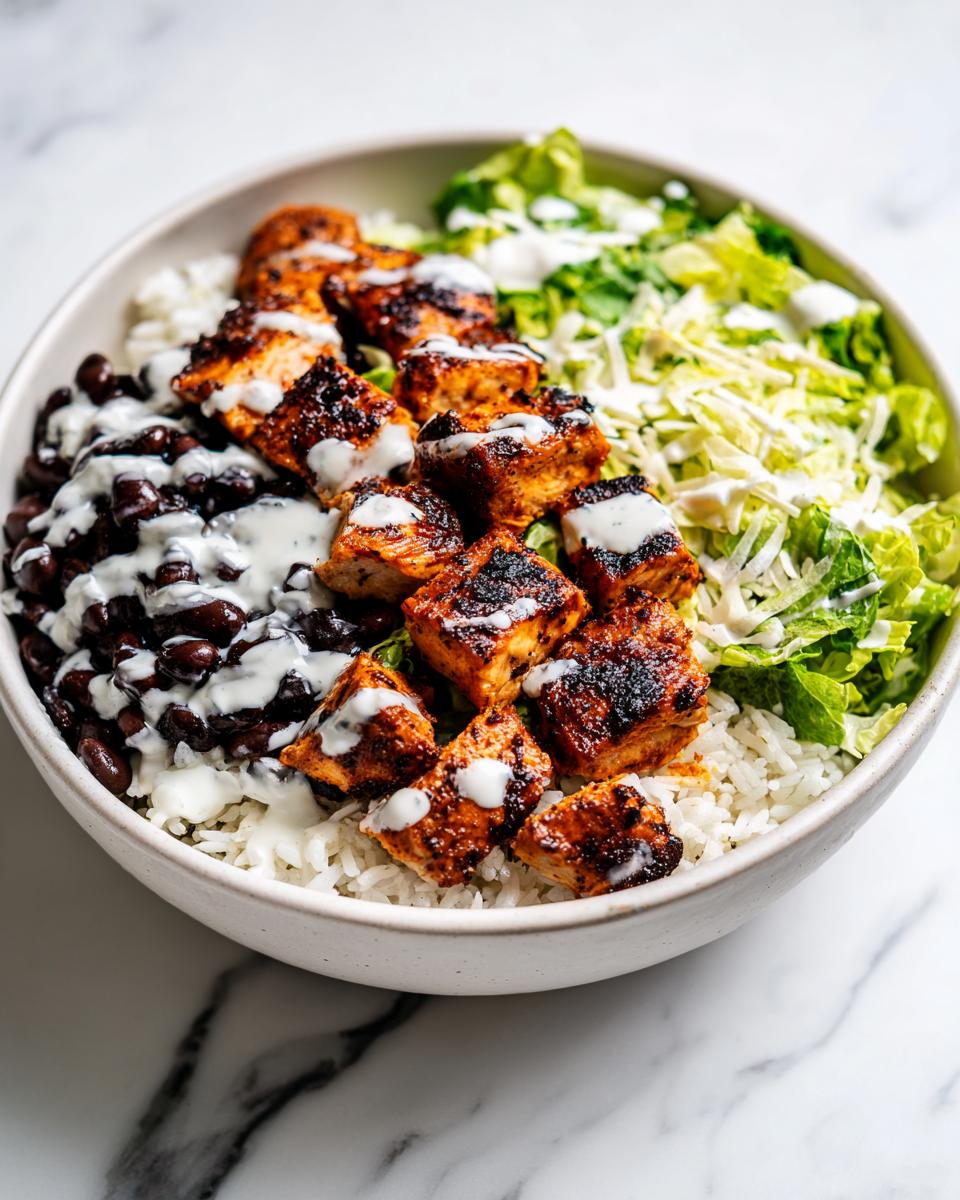 Close-up of a High Protein Chicken Taco Bowl featuring seasoned chicken, black beans, rice, lettuce, and a white drizzle.