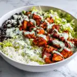 A vibrant High Protein Chicken Taco Bowl featuring seasoned chicken, rice, black beans, lettuce, and a creamy green sauce.
