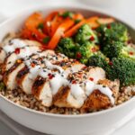 Close-up of a High Protein Summer Chicken Bowl featuring sliced grilled chicken, brown rice, broccoli, carrots, and white sauce.