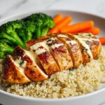 Sliced, seasoned chicken breast drizzled with sauce, served over quinoa with steamed broccoli and carrots for a High Protein Summer Chicken Dinner.