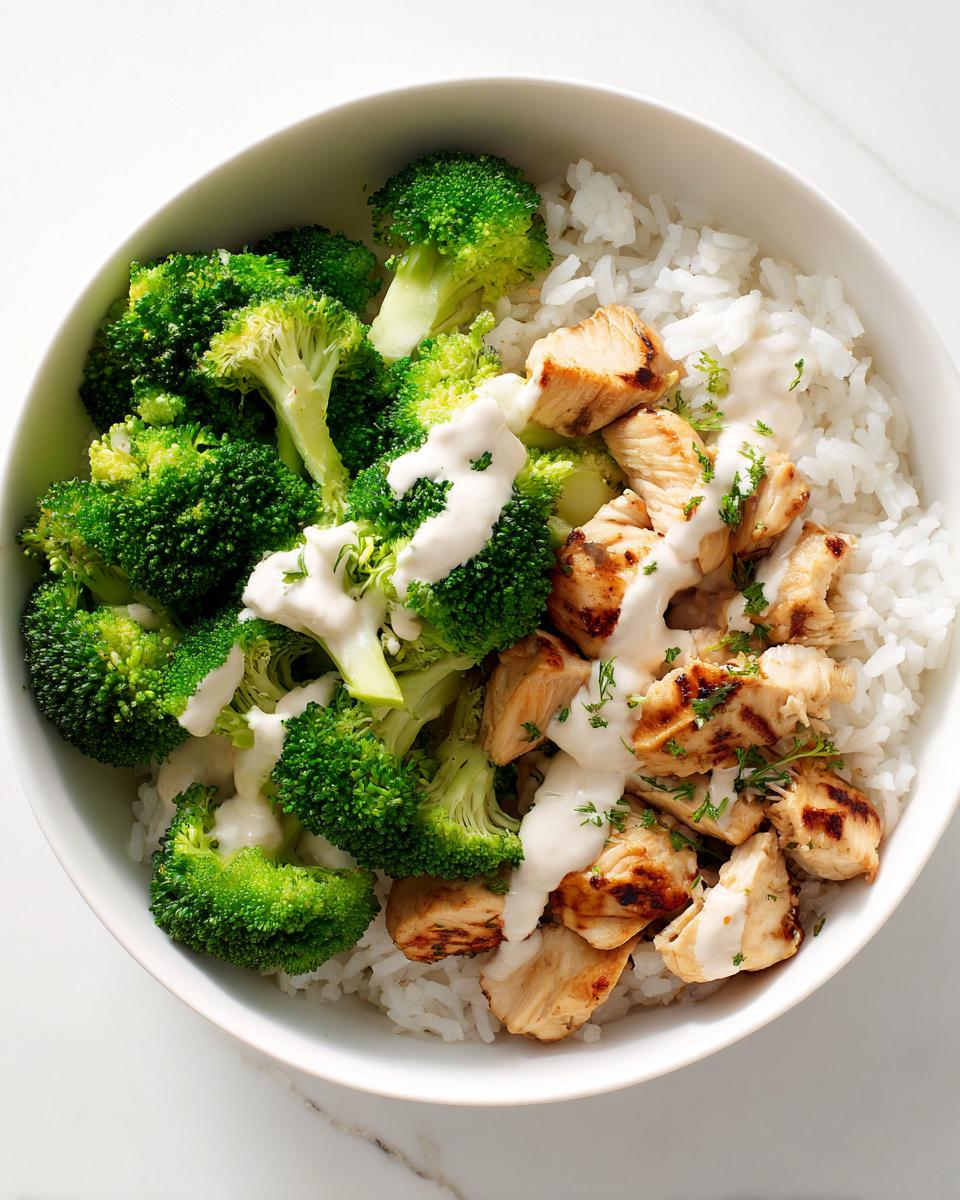 Overhead view of a bowl containing rice, grilled chicken, steamed broccoli, and a white sauce, perfect for High Protein Summer Meal Prep.