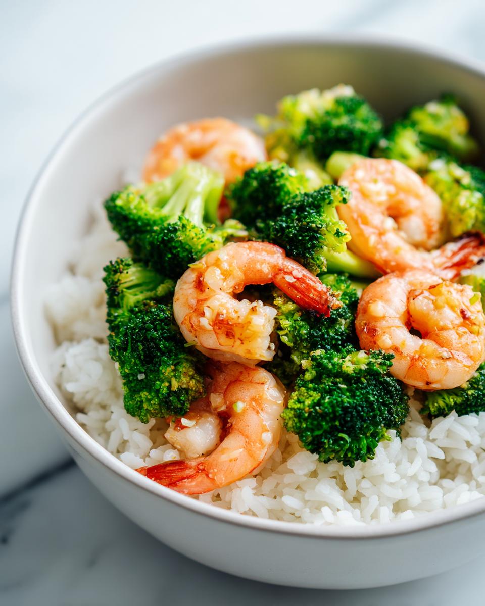 Close-up of a white bowl containing white rice topped with bright green broccoli florets and seasoned shrimp for a High Protein Summer Shrimp Bowl.