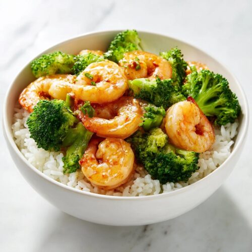 Close-up of a white bowl filled with white rice, topped with glazed shrimp and bright green broccoli florets for a High Protein Summer Shrimp Bowl.
