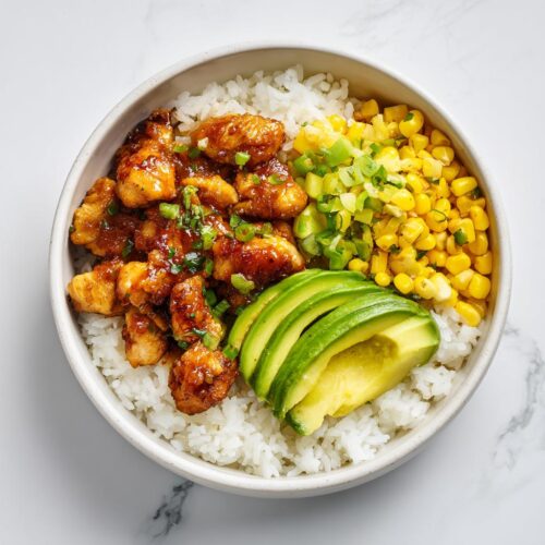 A vibrant Honey Lime Chicken Summer Bowl featuring glazed chicken pieces over white rice, topped with sliced avocado, corn, and green onions.