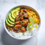 A vibrant Honey Lime Chicken Summer Bowl featuring glazed chicken, white rice, sliced avocado, corn, and lime wedges.