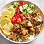 Close-up overhead view of a Lemon Chicken Summer Bowl served over white rice with fresh lemon slices, chopped tomatoes, and cucumbers.
