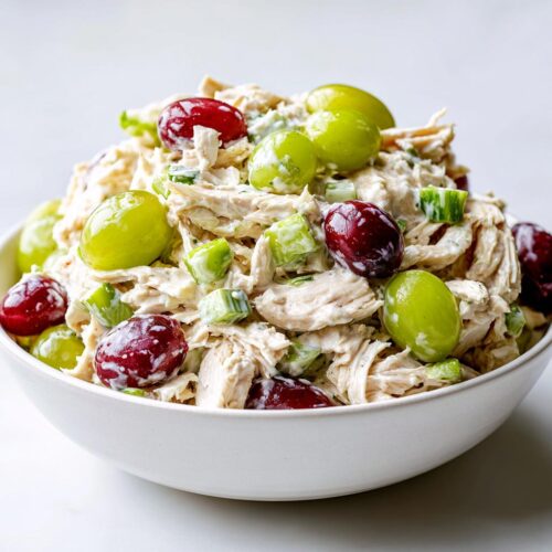 Close-up of a bowl filled with Light Summer Chicken Salad featuring shredded chicken, celery, and whole red and green grapes.