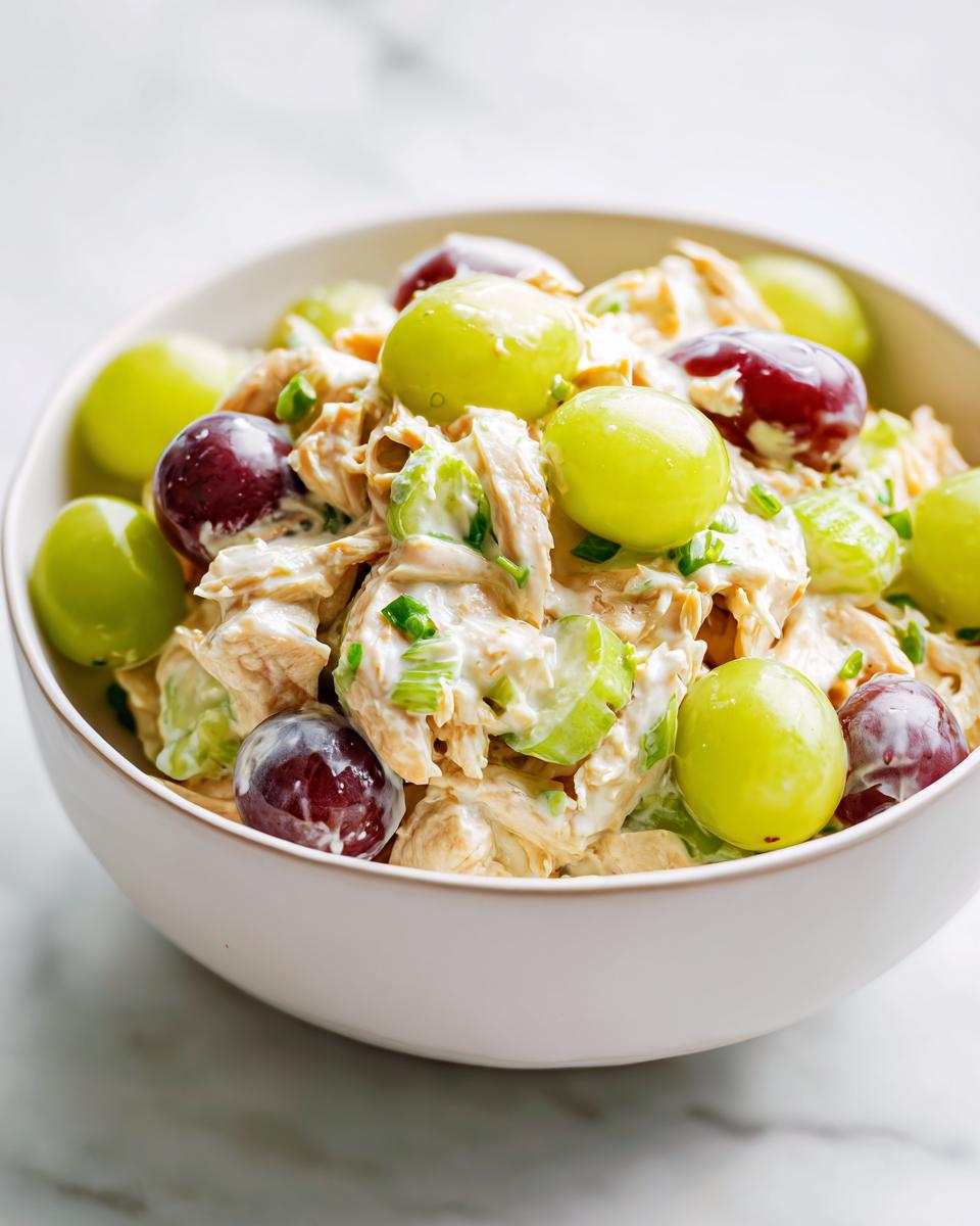 Close-up of creamy Light Summer Chicken Salad mixed with red and green grapes in a white bowl.