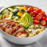 Close-up of a vibrant Light Summer Dinner Bowl featuring sliced grilled chicken, quinoa, avocado, grilled zucchini, and cherry tomatoes.