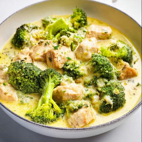 Close-up of Low Carb Creamy Chicken with Broccoli in a white bowl, covered in rich yellow sauce.