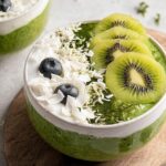 Close-up of a bowl of bright green Matcha Overnight Oats topped with sliced kiwi, blueberries, and coconut flakes.