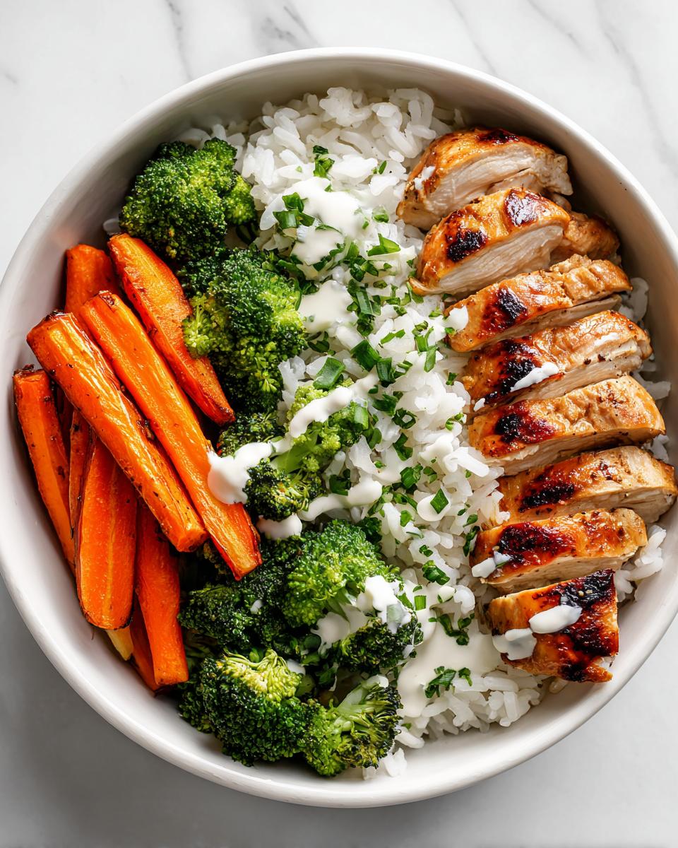 Overhead view of a Meal Prep Summer Dinner Bowls featuring sliced grilled chicken, white rice, roasted carrots, and broccoli with a white sauce.