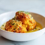 Three golden-brown chicken meatballs served in a creamy yellow sauce, garnished with herbs, perfect for Summer Dinner Easy Recipes.