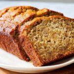 Close-up of a freshly baked Moist Banana Bread Loaf, partially sliced, showing its tender, golden crumb texture.